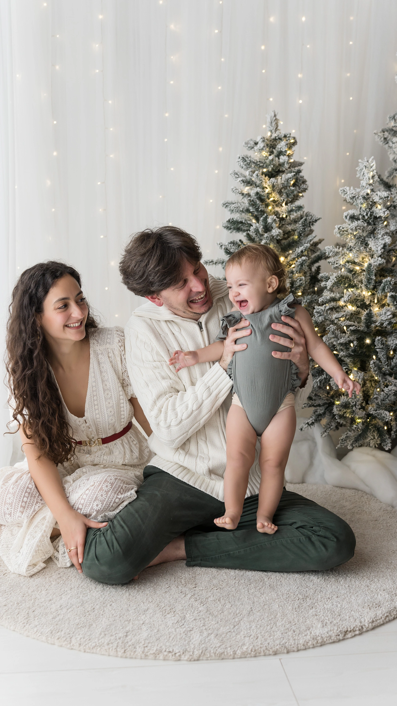 Mamma e papà baciano i loro due bambini sul divano crema, set di Natale dell’Atelier a Livorno