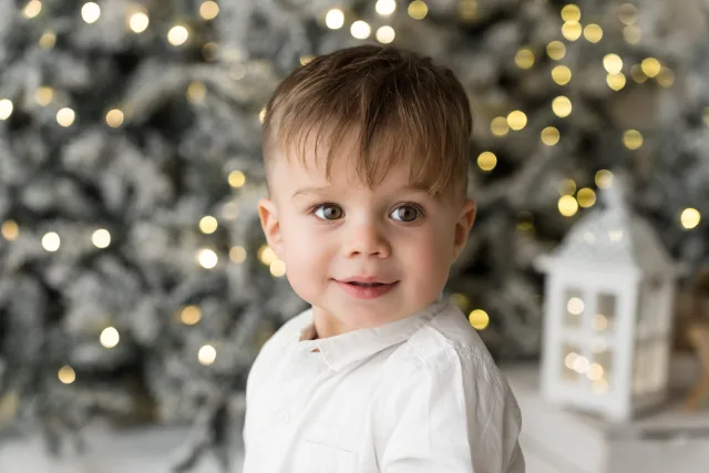 Primo piano di un bambino che sorride davanti all’albero illuminato