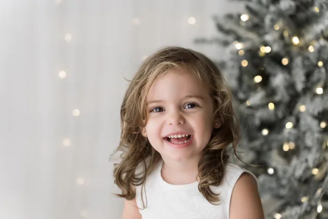 Bambina che sorride davanti all’albero innevato, mezzobusto