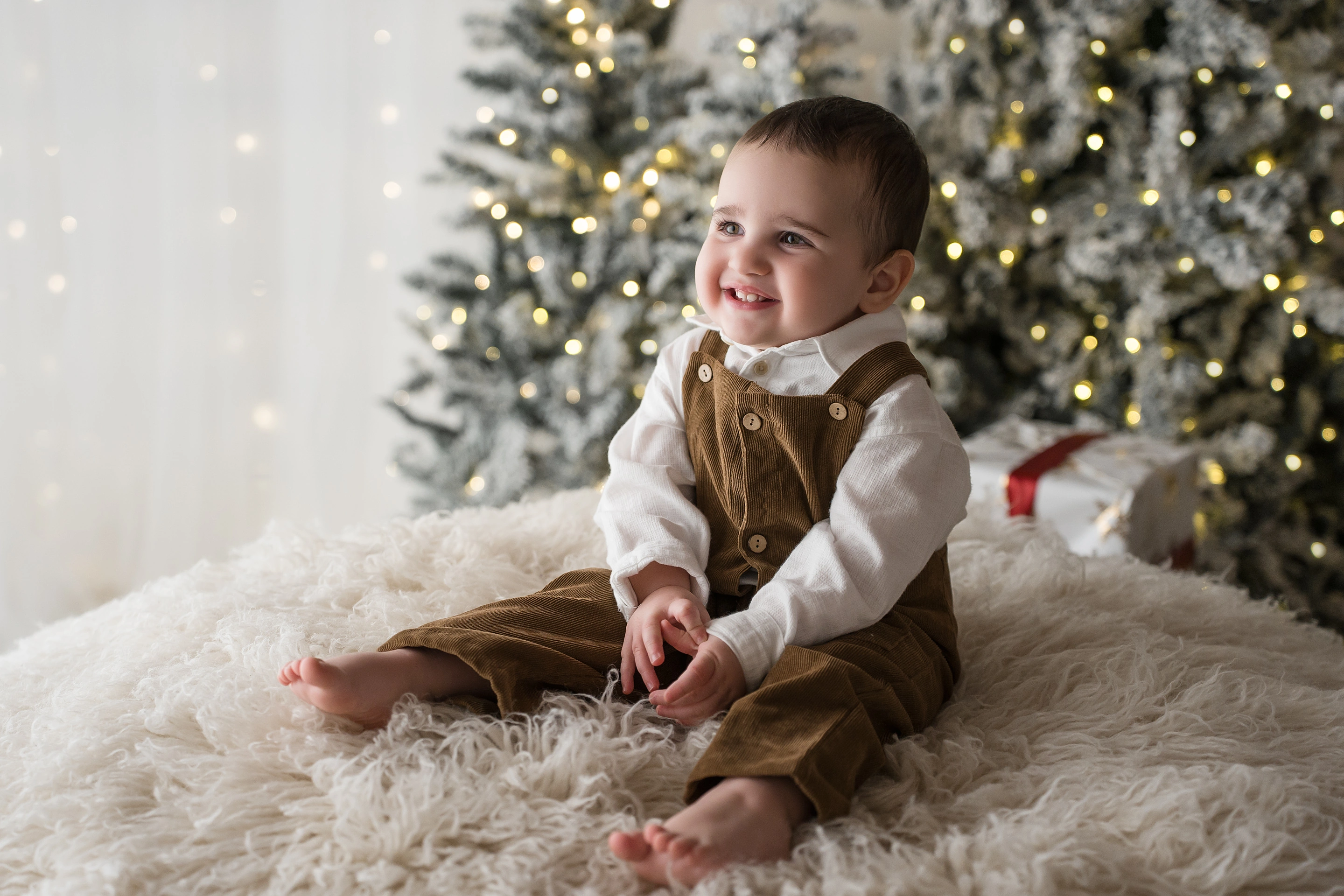 Bambina seduta nella slitta bianca davanti all’albero innevato, set di Natale a Livorno