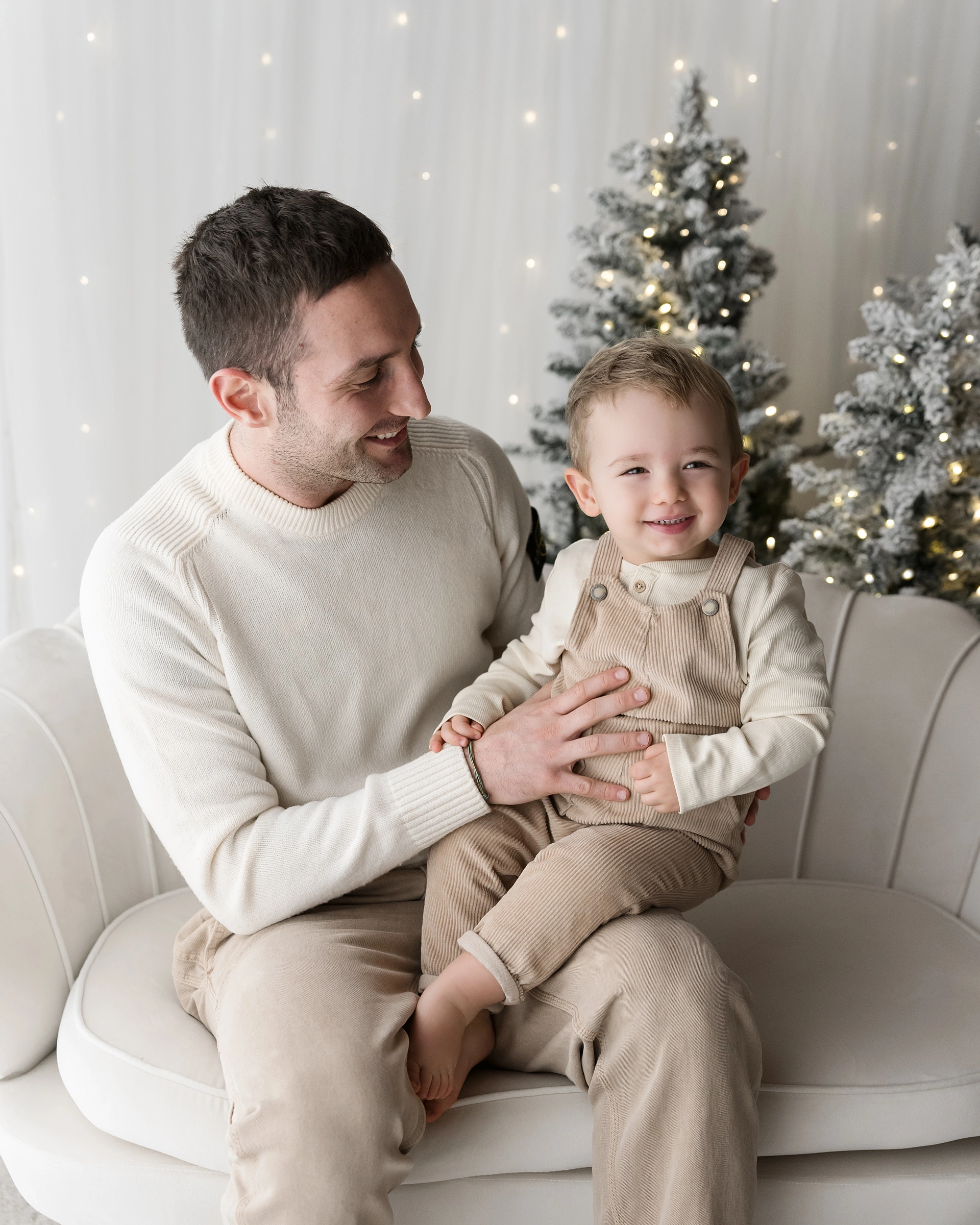 Famiglia di quattro sulla poltrona crema con l’albero di Natale e i regali, Atelier di Livorno