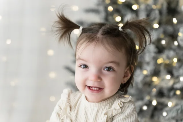 Bambina con i codini che sorride davanti alle lucine dell’albero