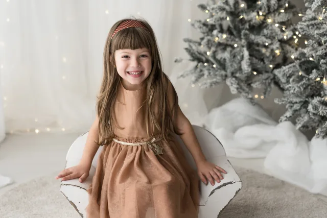 Bambina con l’abito cipria in piedi davanti all’albero di Natale