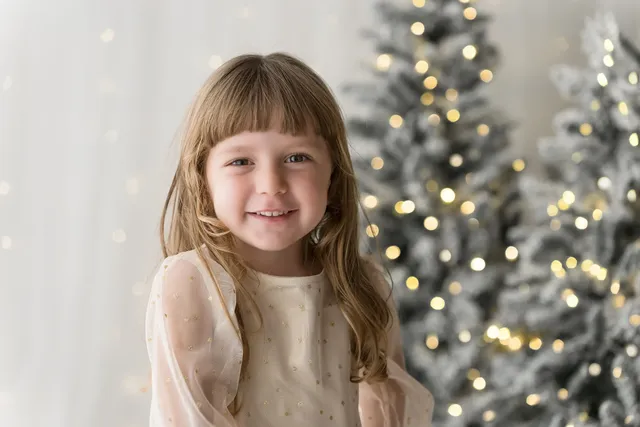 Bambina sorridente davanti all&rsquo;albero innevato, mezzobusto