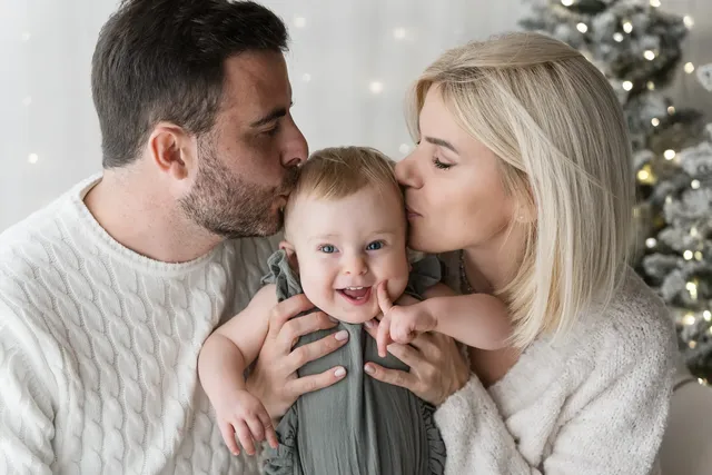Mamma e pap&agrave; baciano sulle guance il loro bambino nel set di Natale